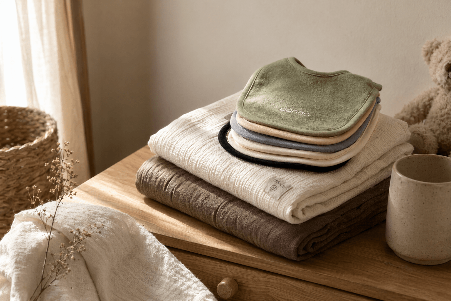 Folded dánda cotton essentials in calm tones on a quiet nursery shelf